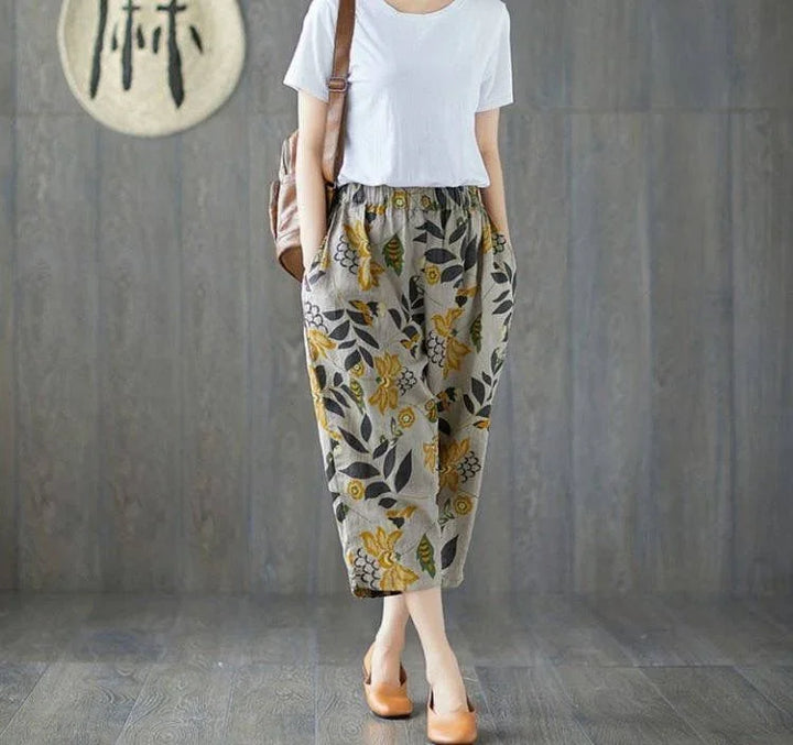 Woman in white t-shirt and floral patterned loose pants with pockets, wearing tan heels, brown bag