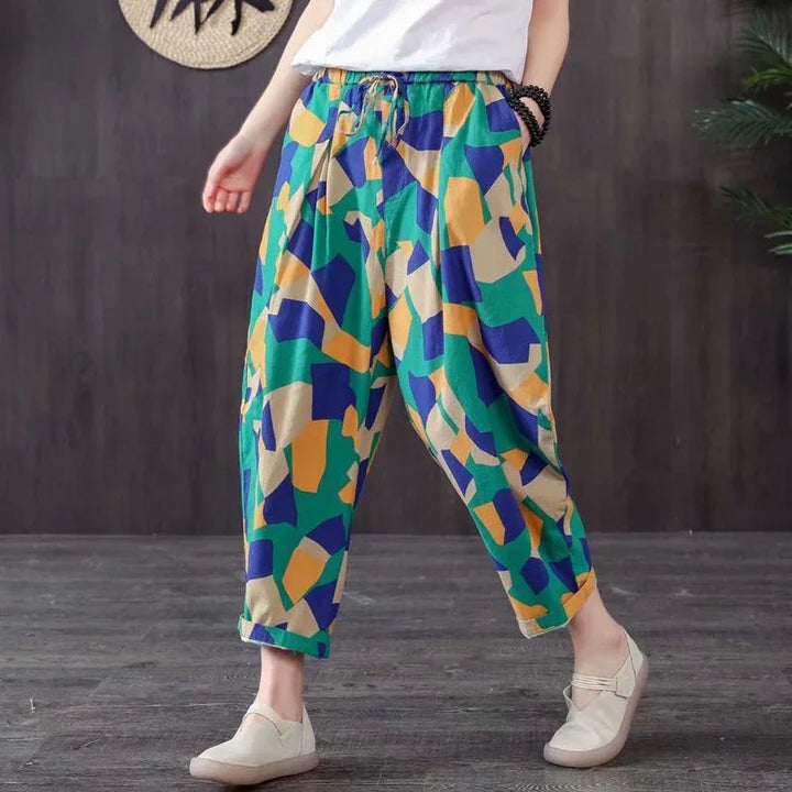 Person wearing colorful geometric print baggy pants and white slip-on shoes on wooden floor