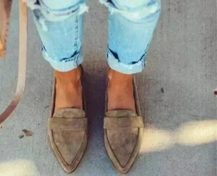 Person wearing beige pointed suede loafers and cuffed light blue ripped jeans on concrete floor