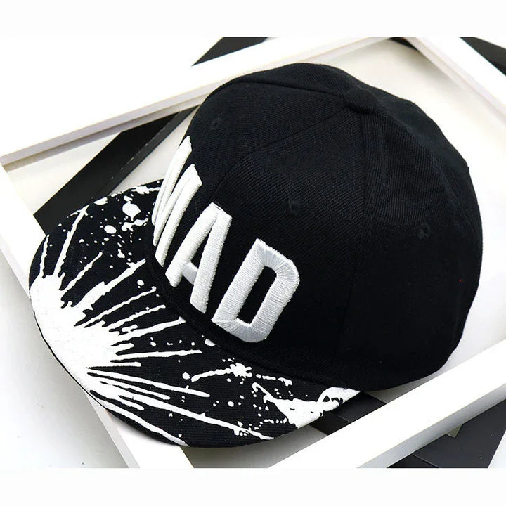Black snapback cap with white splatter design on brim and bold white embroidered MAD letters