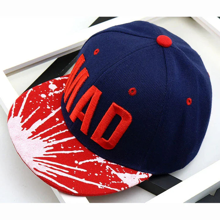 Navy blue snapback cap with red embroidered word MAD and red-white splatter pattern on visor