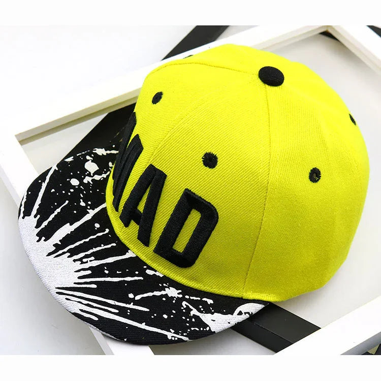 Bright yellow snapback cap with black embroidered text and black and white paint splatter brim