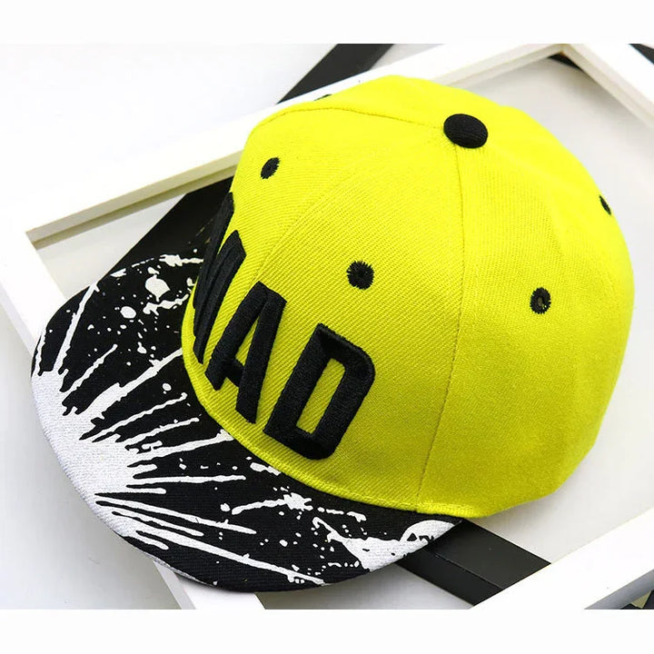 Bright yellow snapback cap with black embroidered text and black and white paint splatter brim