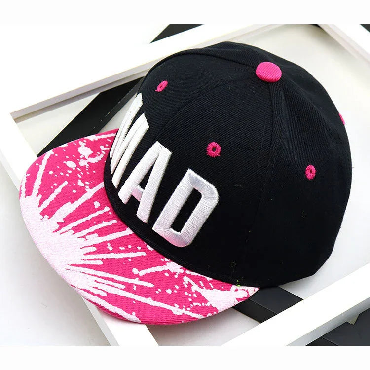 Black snapback cap with large white MAD text and pink and white splatter design on the flat brim