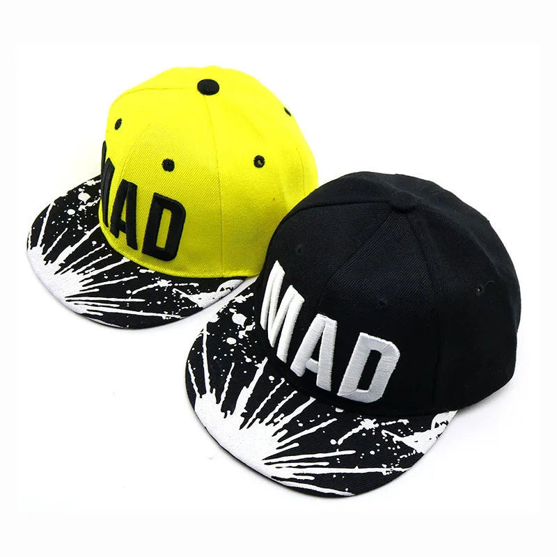Two snapback caps with graffiti-style black and white brims, one yellow and one black, both with bold 'MAD' lettering