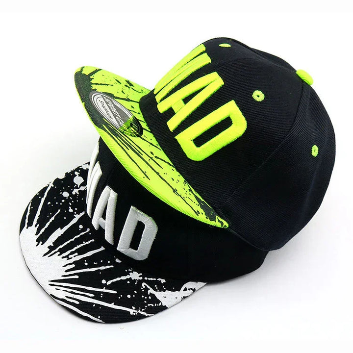 Two snapback caps with 'MAD' embroidery, one with neon green cracked pattern, one with black and white splatter design