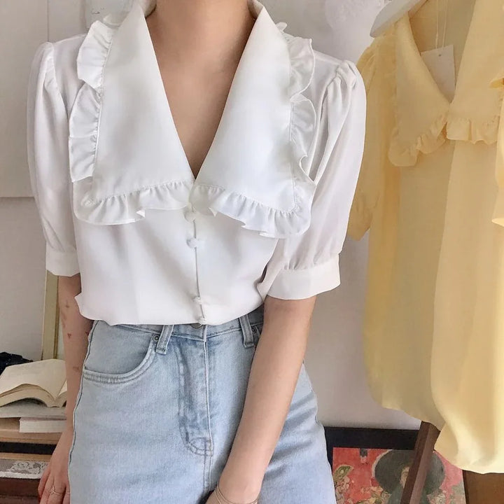 Woman wearing white blouse with ruffled wide collar and short puff sleeves paired with high-waisted light blue jeans