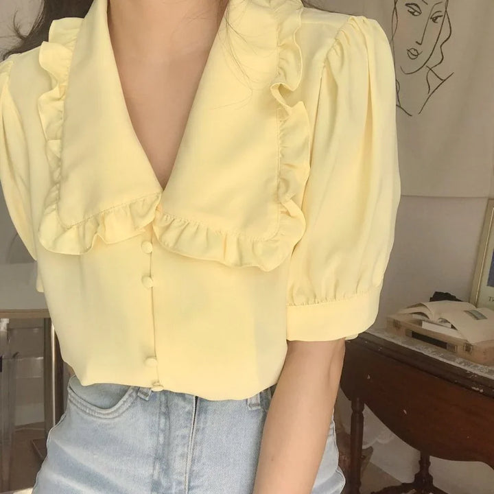 Close-up of woman wearing light yellow ruffle collar blouse with puff sleeves and light blue jeans indoors
