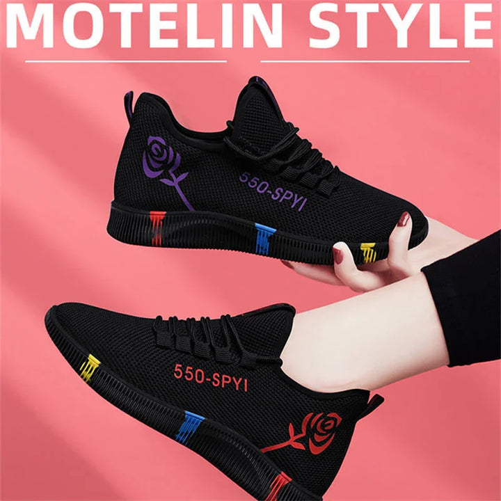 Black lightweight sneakers with colorful accents and rose design, worn on feet against pink background