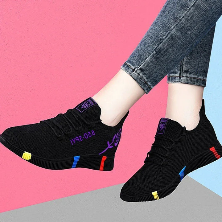Black casual sneakers with colorful sole accents and purple rose details worn with rolled-up jeans on pink and blue background