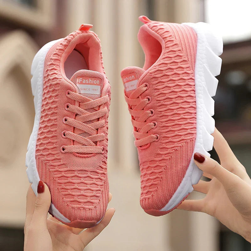 Pink knitted lightweight sports shoes with white soles held in hands, casual fashion sneakers