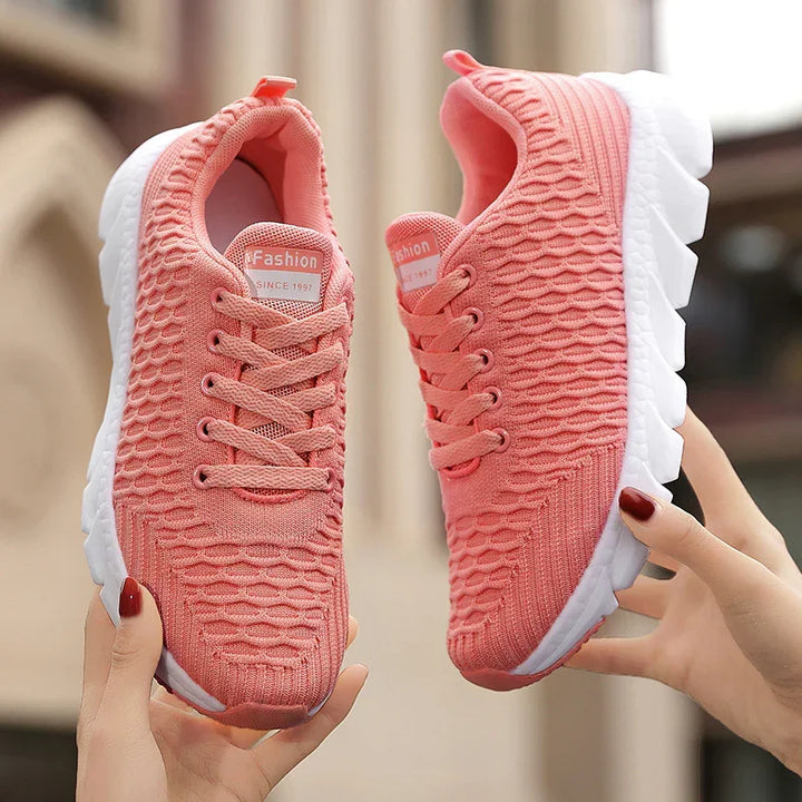 Pink knitted lightweight sports shoes with white soles held in hands, casual fashion sneakers