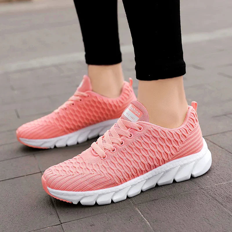 Close-up of pink textured knit sneakers with white chunky soles worn with black leggings on pavement