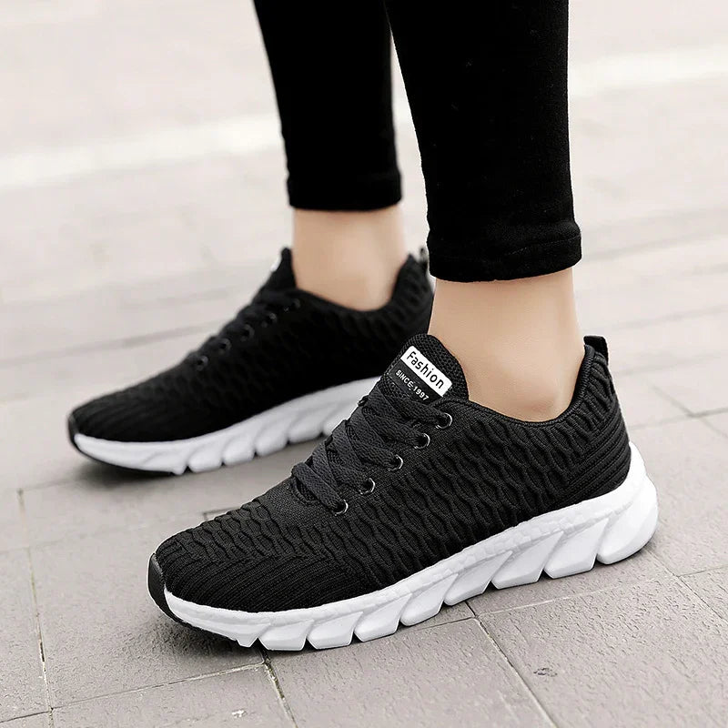 Black knit fashion sneakers with thick white soles worn with black leggings on pavement