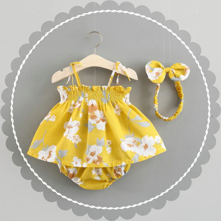 Yellow floral baby dress with matching headband on wooden hanger against gray background