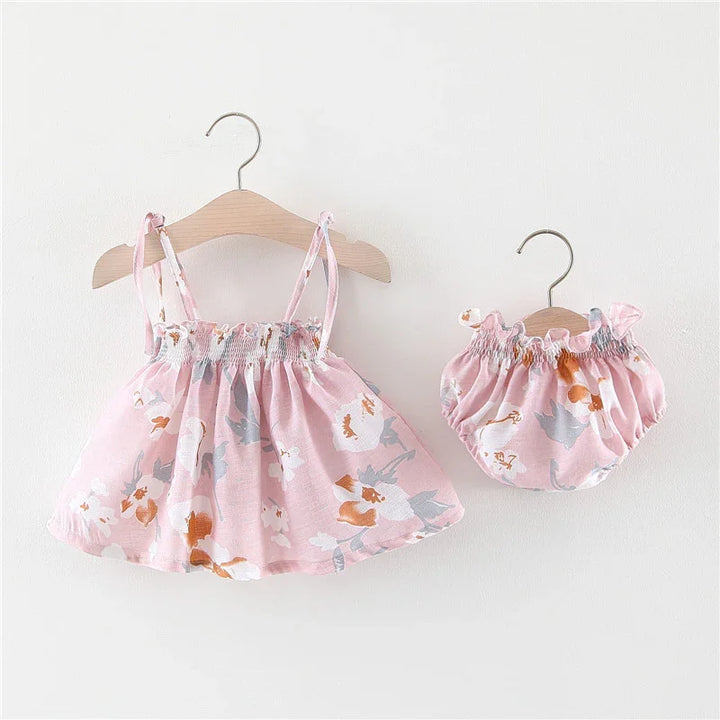 Pink floral baby dress and matching bloomers with ruffle details on wooden hangers