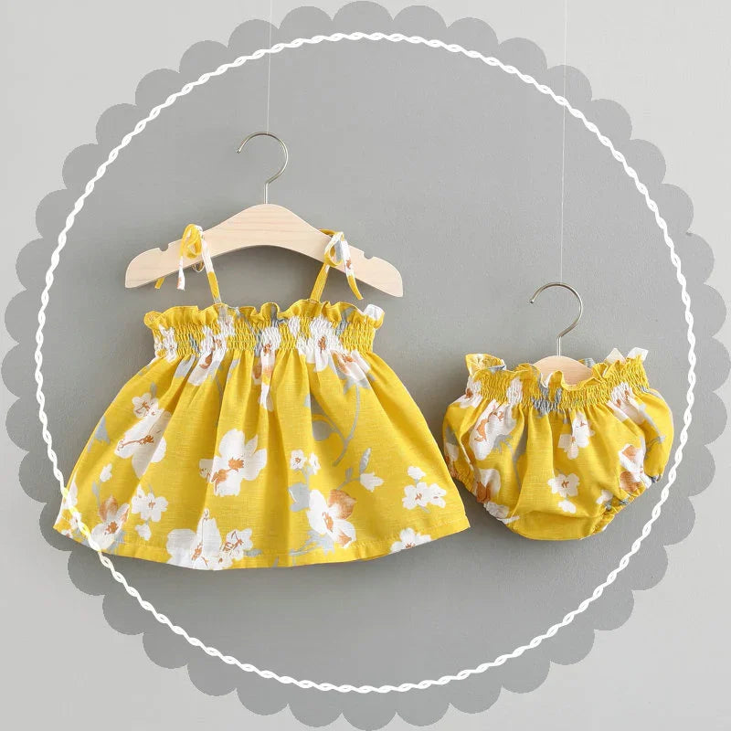 Yellow floral baby dress and matching bloomers on wooden hangers with gray background
