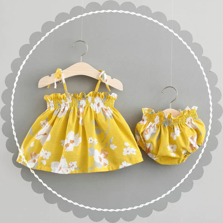 Yellow floral baby dress and matching bloomers on wooden hangers with gray background