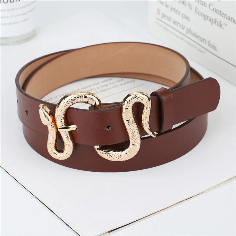 Brown leather belt with gold snake-shaped buckle on white surface with books