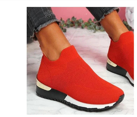 Stylish bright red knit slip-on sneakers with black and white soles worn with frayed black jeans