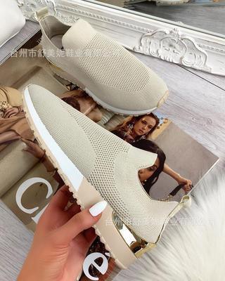 Beige slip-on knit sneakers with white soles and gold accents on a wooden floor with fashion magazine background