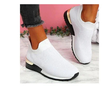White knit slip-on sneakers with black soles and gold accents worn with black frayed jeans