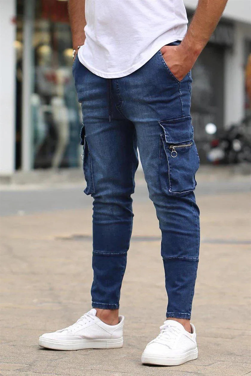 Man wearing dark blue slim-fit cargo jeans with zipper pockets and white sneakers on a street