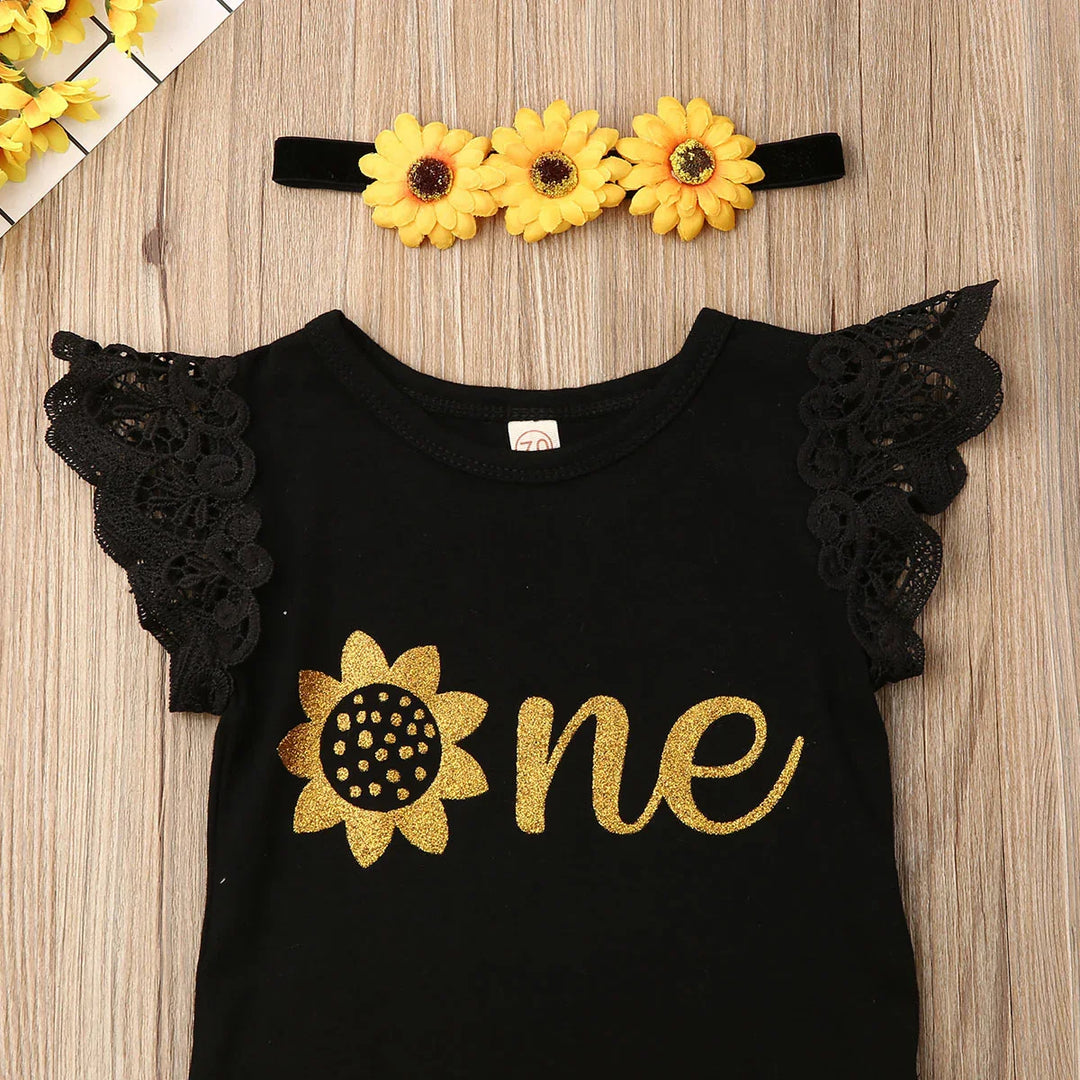 Black baby outfit with gold glitter sunflower print and lace sleeves, yellow sunflower headband on wood