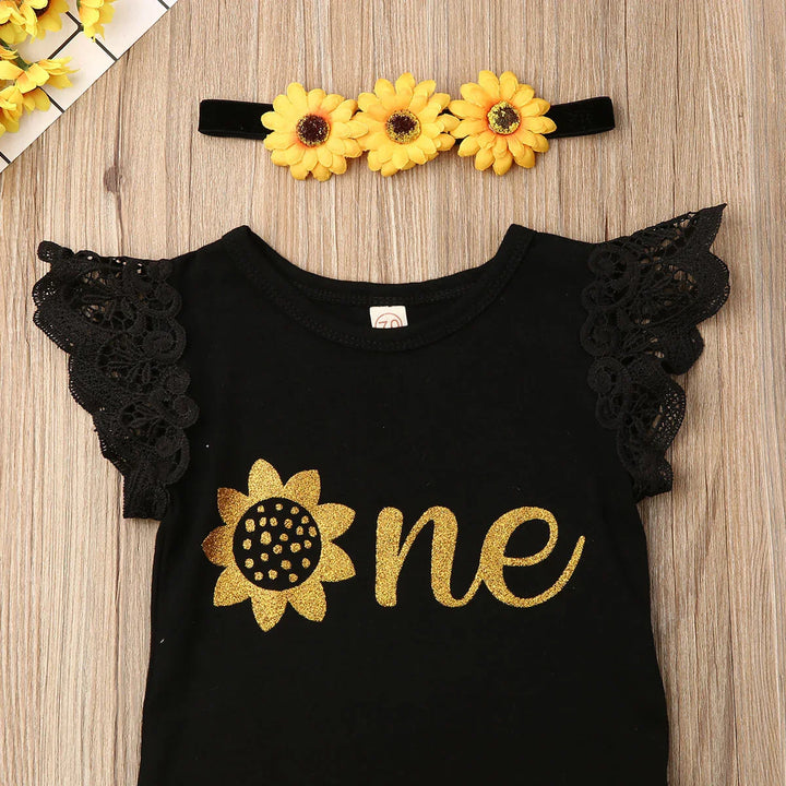 Black baby outfit with gold glitter sunflower print and lace sleeves, yellow sunflower headband on wood