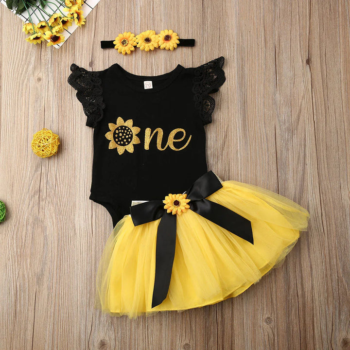 Black baby bodysuit with gold sunflower and word one, yellow tulle skirt with black bow, and sunflower headband