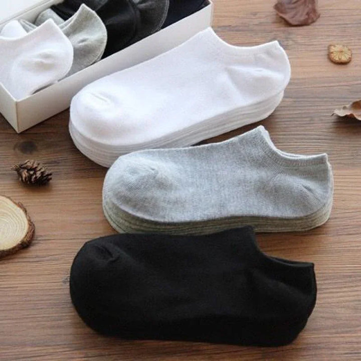 Stack of white, gray, and black ankle socks on wooden surface with natural decor elements