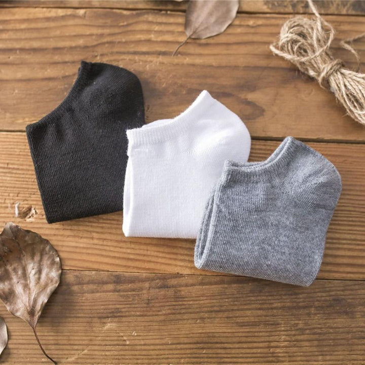 Folded black, white, and gray ankle socks on wooden surface with dried leaves and twine