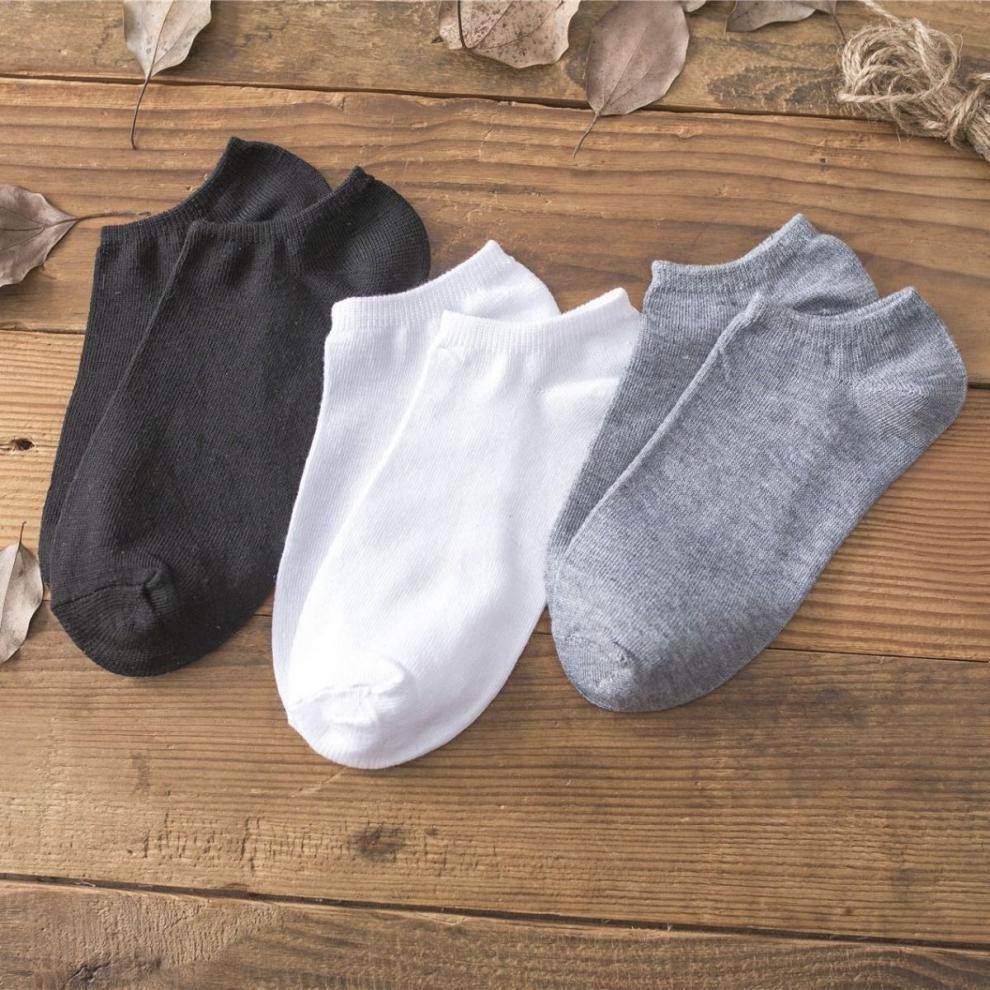 Three pairs of ankle socks in black, white, and gray on wooden surface with dried leaves