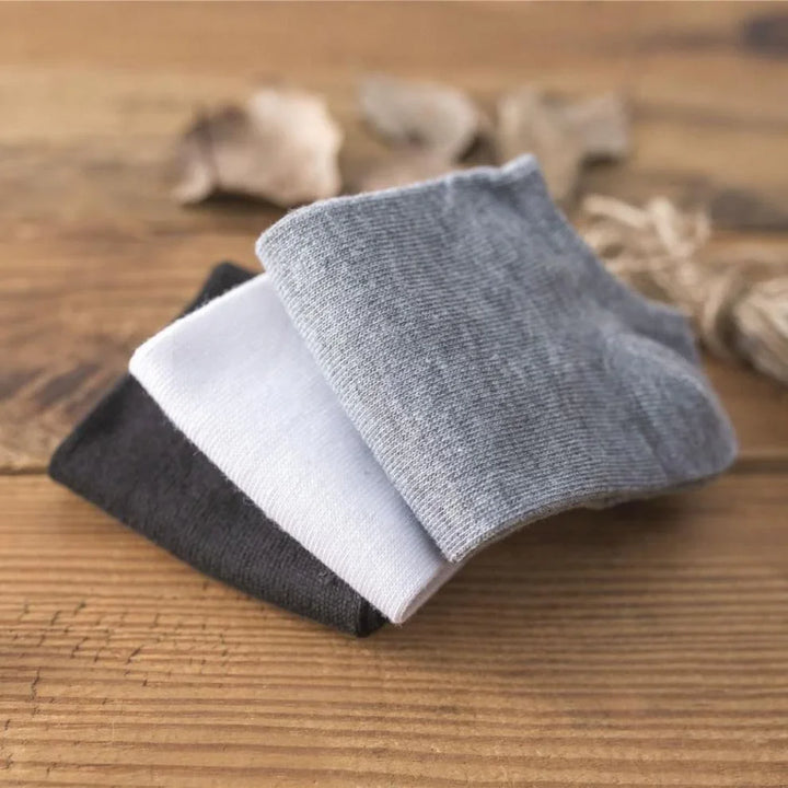 Three pairs of folded ankle socks in gray, white, and black on rustic wooden surface