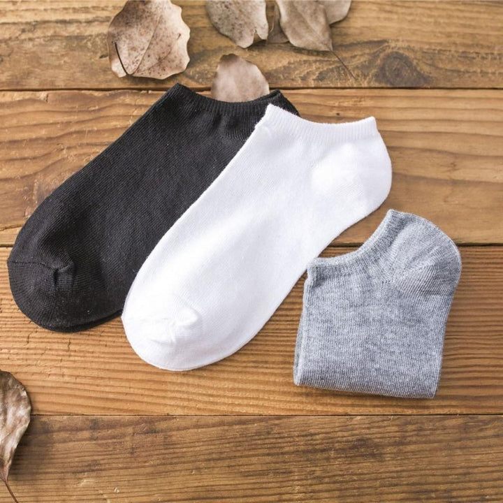 Black, white, and gray ankle socks on wooden surface with dried leaves background