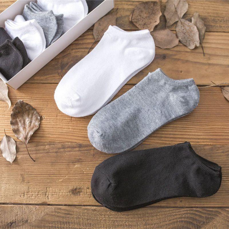 Set of white, gray, and black ankle socks displayed on wooden surface with dried leaves