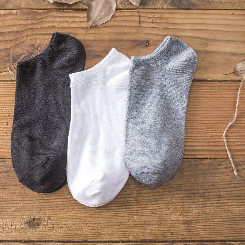 Three pairs of ankle socks in black, white, and gray on wooden surface with dried leaves