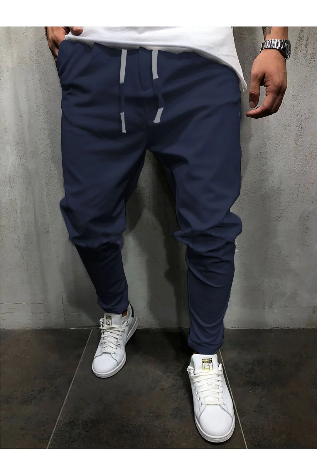 Man wearing navy jogger pants with gray drawstrings and white sneakers against a gray textured wall