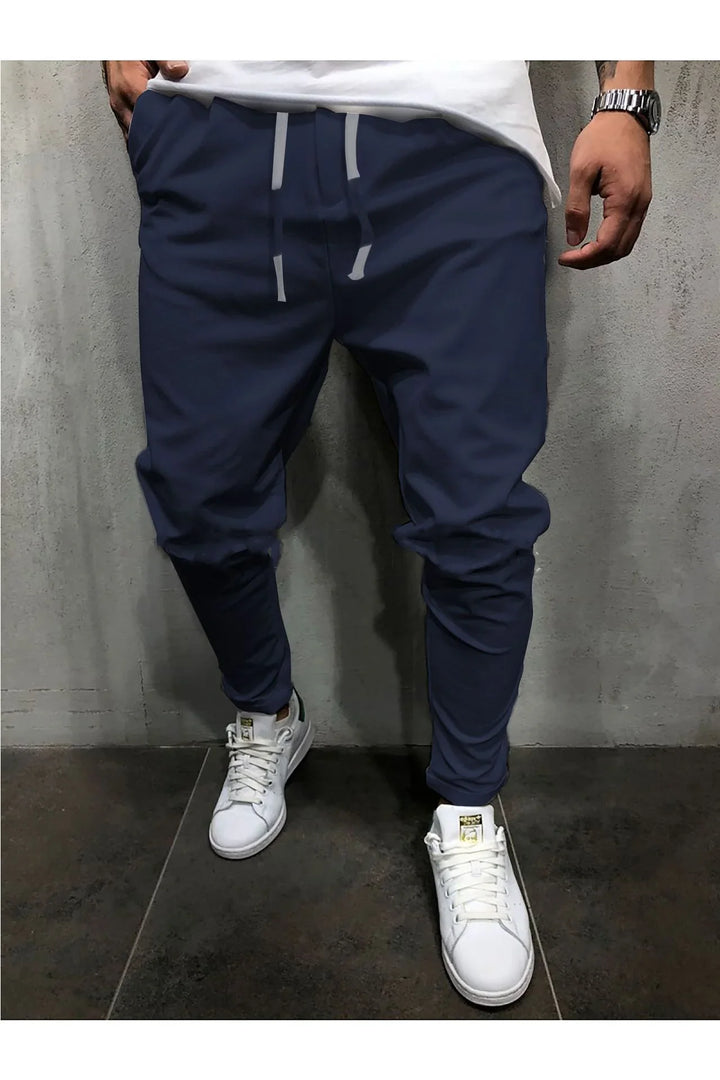 Man wearing navy jogger pants with gray drawstrings and white sneakers against a gray textured wall