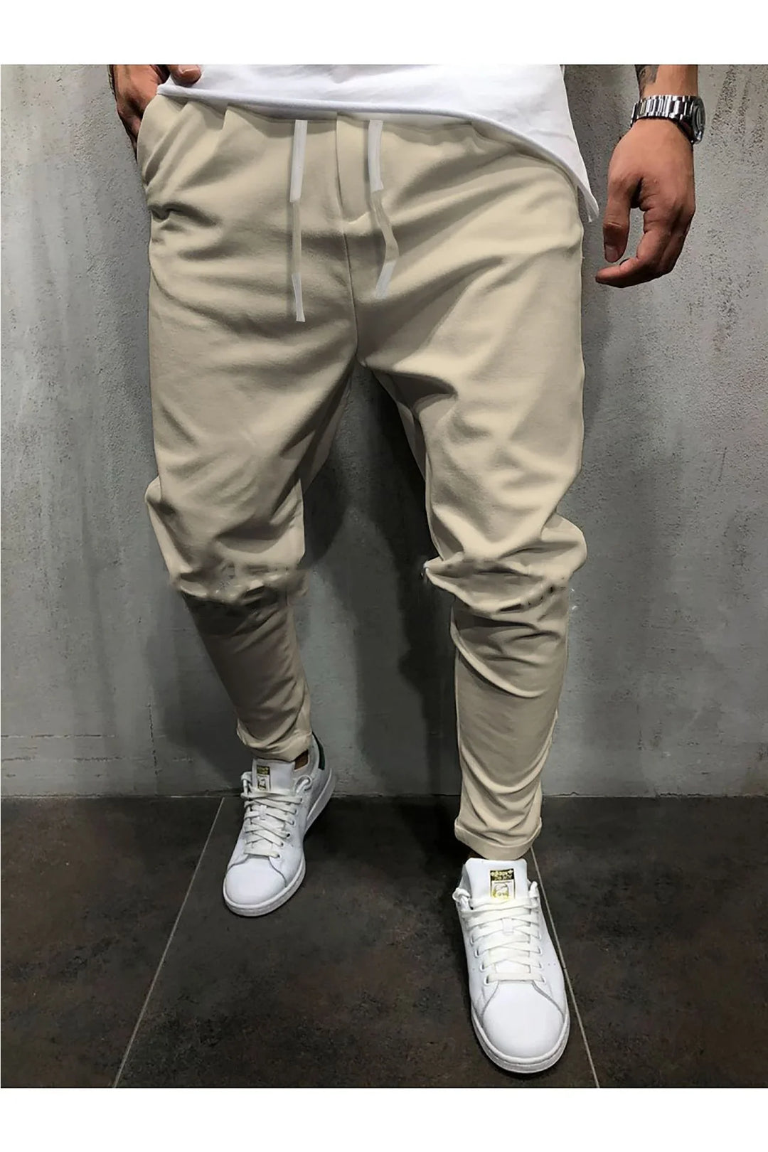 Man wearing beige tapered jogger pants and white sneakers standing against textured wall