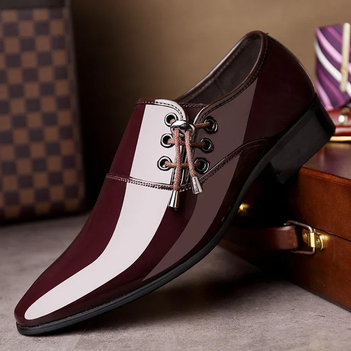 Glossy burgundy men's dress shoe with metal-tipped laces on brown suitcase