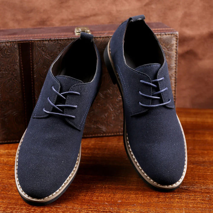 Pair of navy blue suede casual shoes with laces on wooden surface and brown textured background