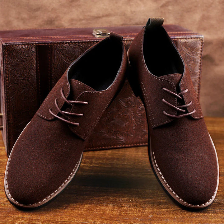 Brown suede men's casual lace-up shoes on wooden surface with embossed leather box background