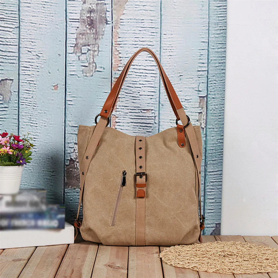 Beige canvas tote bag with brown leather straps on wooden table against rustic blue wall