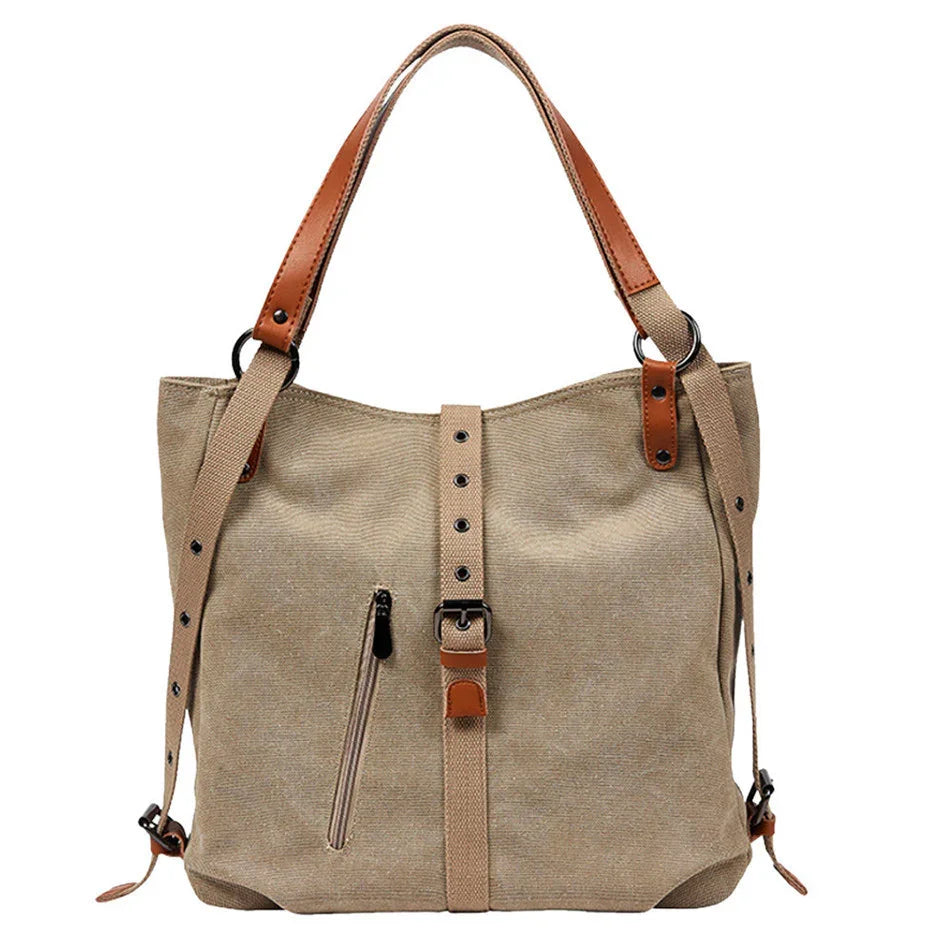 Beige canvas tote bag with brown leather straps, front zipper pocket, and adjustable belt detail