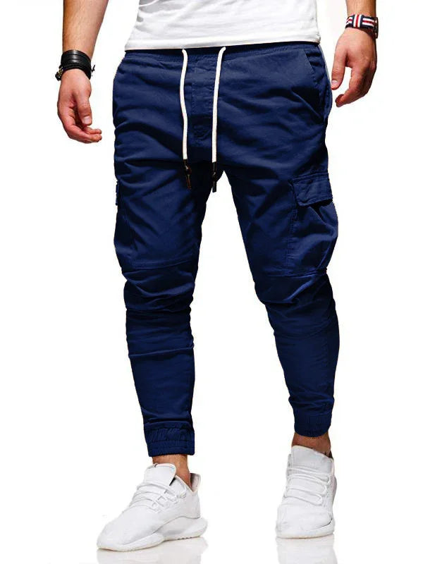 Men's navy blue jogger pants with cargo pockets and white drawstring, paired with white sneakers