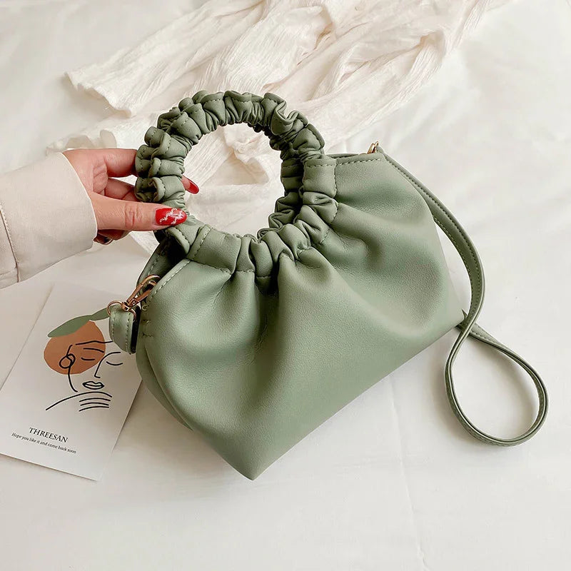 Light green ruched round handle handbag with detachable strap on white fabric backdrop