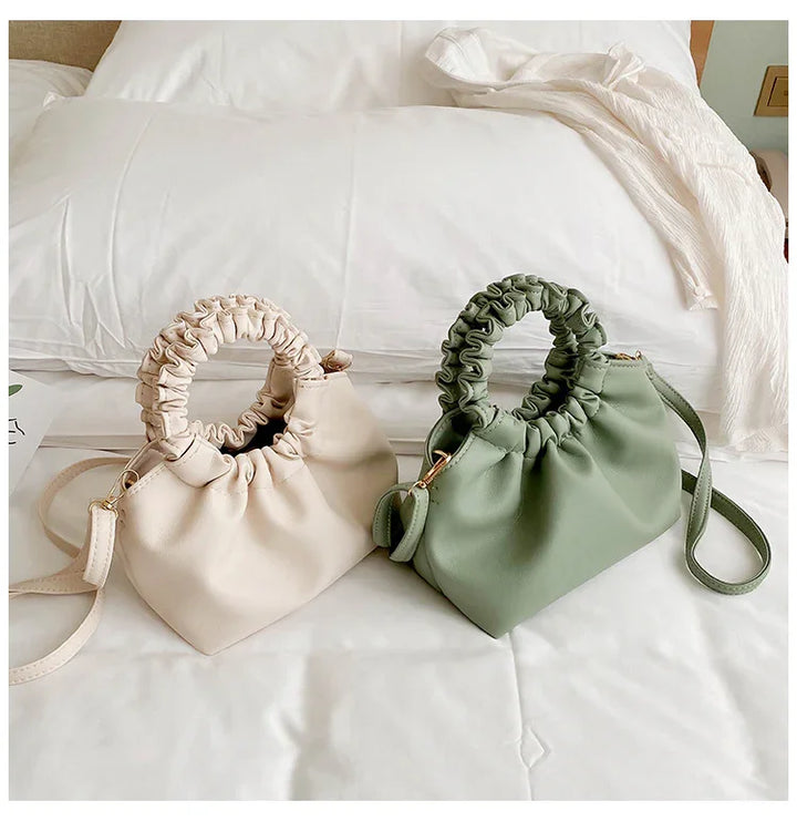 Two stylish ruched handle handbags in beige and sage green displayed on a white bed