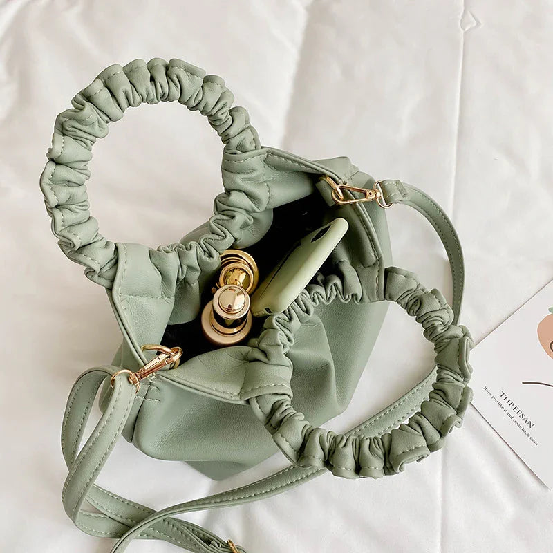 Light green ruched handle handbag with gold hardware, containing lipstick and green smartphone, on white surface