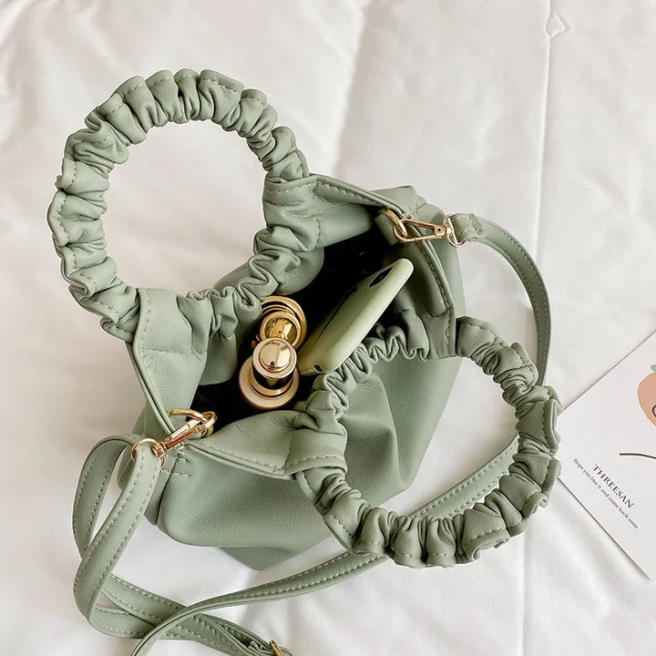 Light green ruched handle handbag with gold hardware, containing lipstick and green smartphone, on white surface